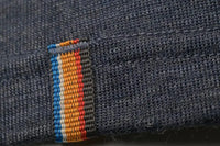 Close-up of the Moggans Merino Short Sleeve Baselayer with TENCEL™ shows its dark blue, moisture-wicking fabric and detailed stitching, plus a label stitched with four vertical stripes in blue, orange, yellow, and red.