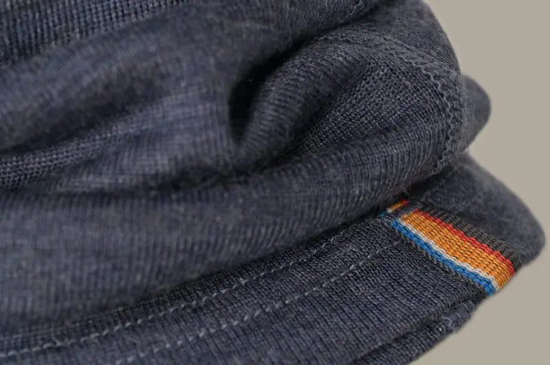 Close-up of a dark blue Moggans Merino Wool Neck Gaiter with TENCEL™ Lyocell, showing breathable fabric, visible stitching, and a small red, yellow, and blue striped detail along one edge.