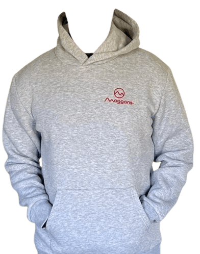 A person wears the Moggans Hoodie – Soft, Warm & Sustainable in light gray, featuring a small red Moggans logo and emblem on the left chest. Hands are in the front pocket against a plain white background.